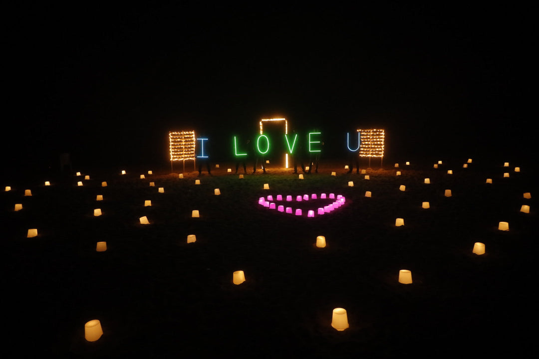 Private beachside anniversary surprise setup with 100 candles along the shore and neon light board – Stars on the Shore by Surprisemachi Chennai