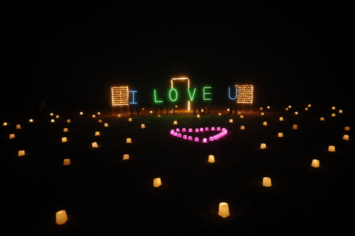 Private beachside anniversary surprise setup with 100 candles along the shore and neon light board – Stars on the Shore by Surprisemachi Chennai